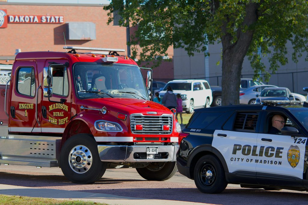 Fire truck and police car parked outside Dakota State University on a sunny day.