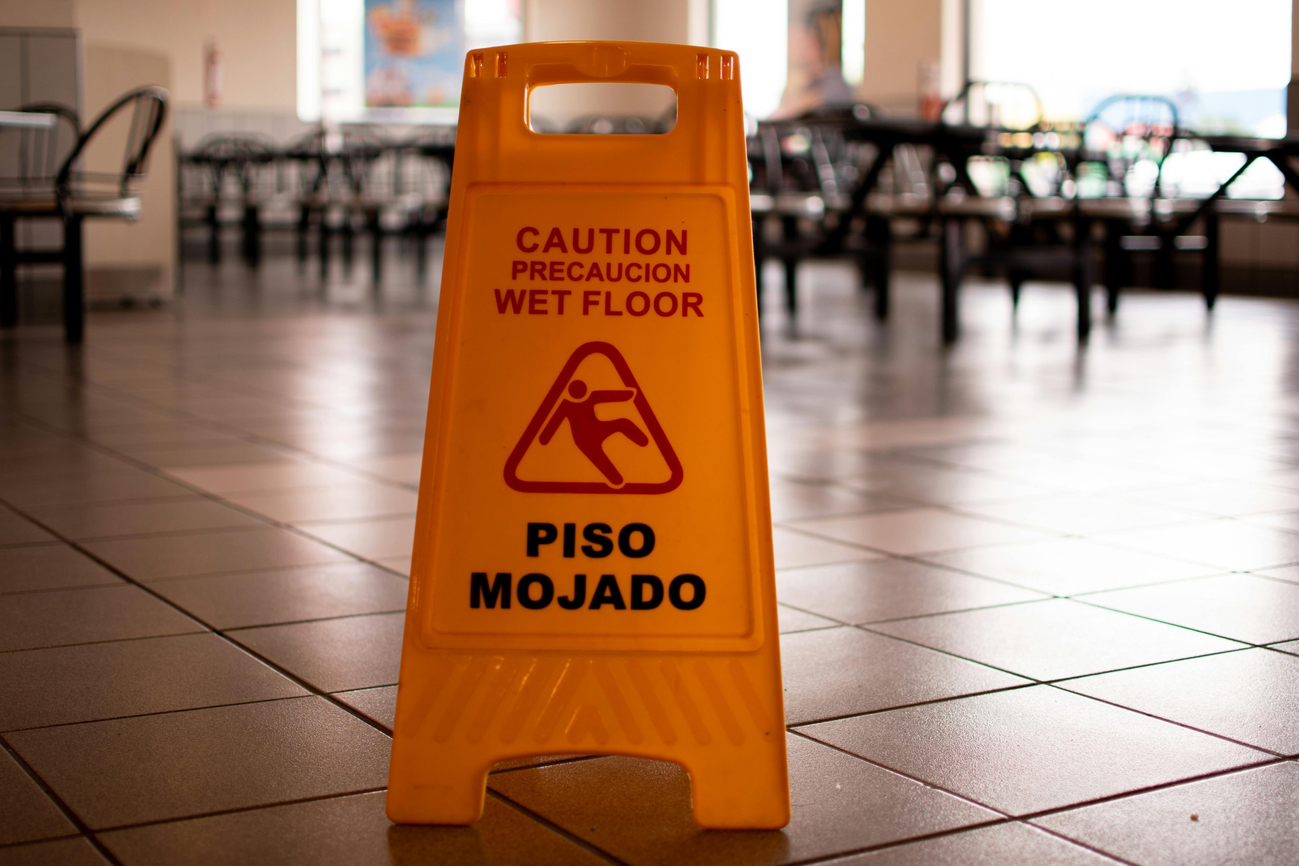 Property & Casualty Yellow caution wet floor sign in a cafeteria warns of slippery conditions on tiled floor.