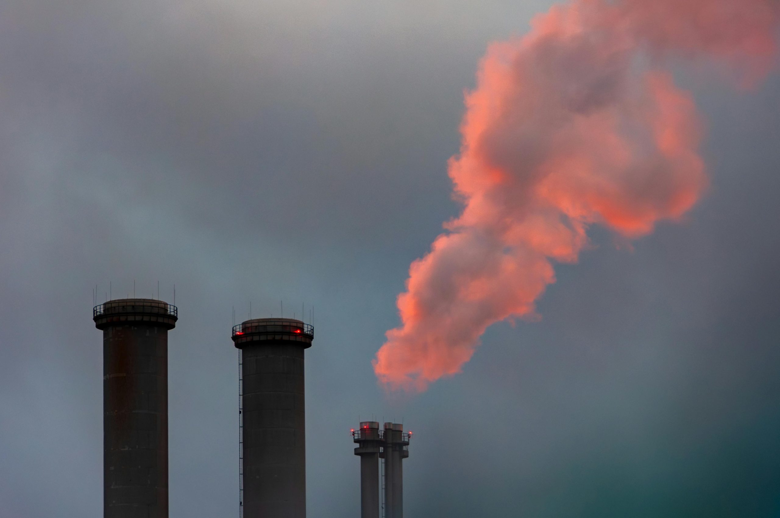 Dramatic industrial scene with chimneys releasing vivid pink smoke into the sky.